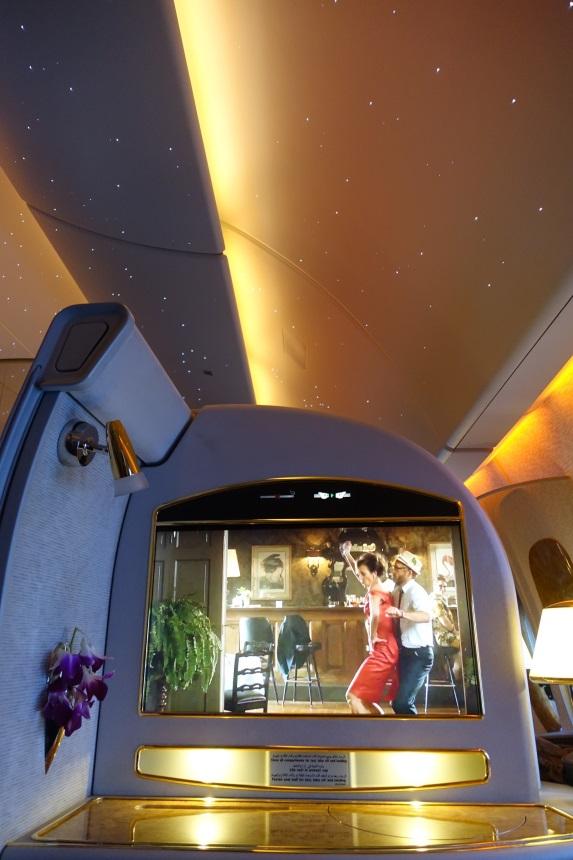 An Emirates First Class suite interior with a movie playing on the entertainment screen and a starry fiber optic ceiling.