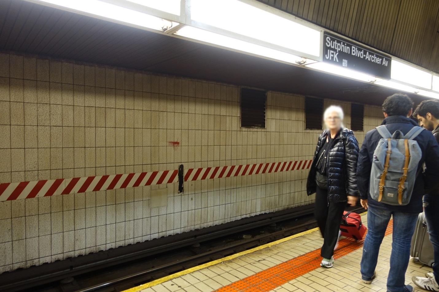 Travelers with luggage wait on the Sutphin Blvd-Archer Av JFK subway platform.