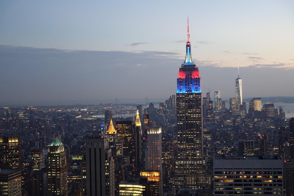 New York City skyline at dusk, with the Empire State Building illuminated in red and blue.