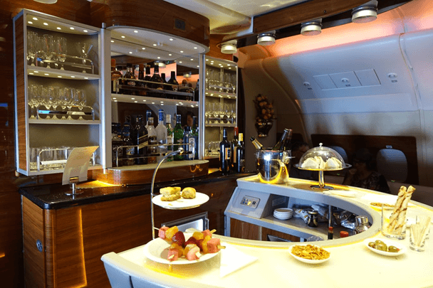 Emirates A380 onboard bar featuring bottles of liquor, glasses, and an array of snacks.