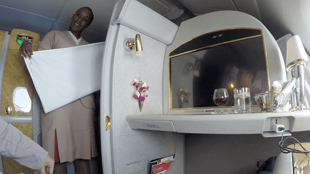 An Emirates flight attendant offers a blanket in a luxurious First Class suite.