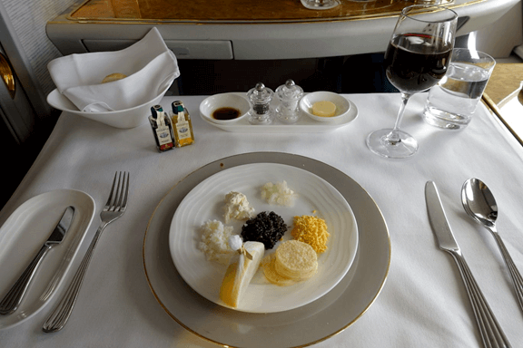 A table is set with caviar, garnishes, wine, and bread in an Emirates First Class cabin.
