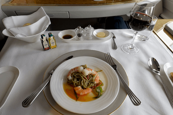 An Emirates First Class meal of shrimp and noodles with red wine and condiments.