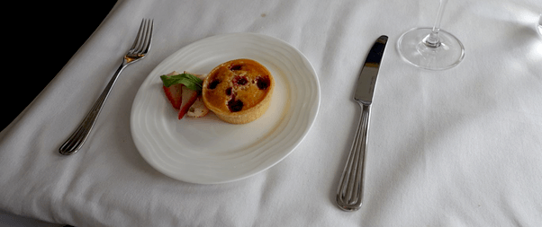 A dessert plate with a small tart, strawberries, and cutlery on a white tablecloth.