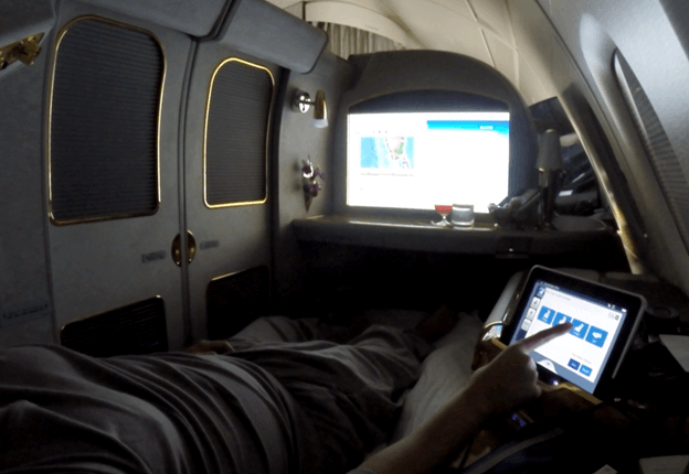 A passenger in an Emirates A380 First Class suite uses a tablet while relaxing in a lie-flat bed.