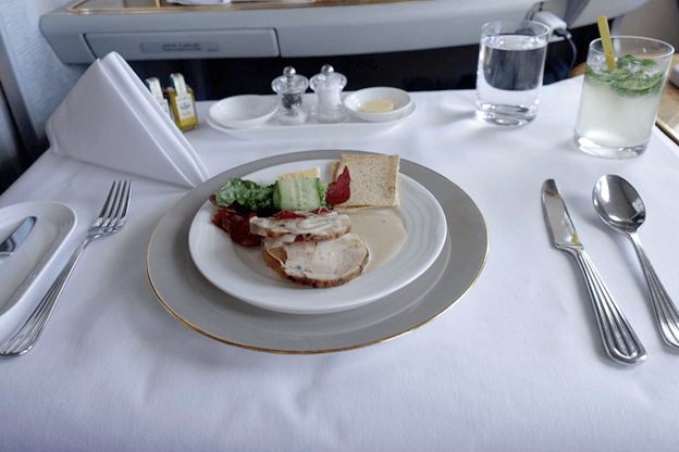 An elegantly plated meal with drinks and silverware served on a white tablecloth in Emirates First Class.