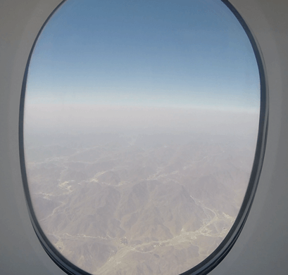 View of a hazy desert landscape and mountains from an airplane window.
