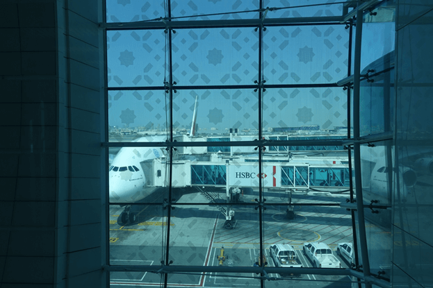 Emirates A380 aircraft parked at a gate, viewed through a patterned airport window.