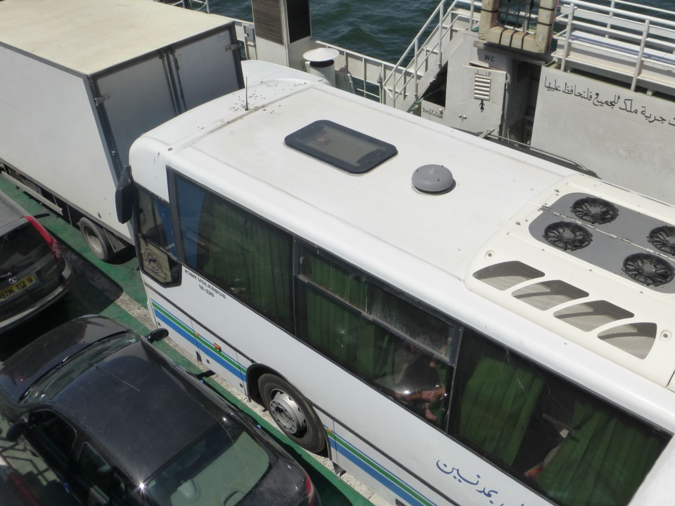 An overhead view of a white bus, a truck, and cars tightly parked on a ferry deck.