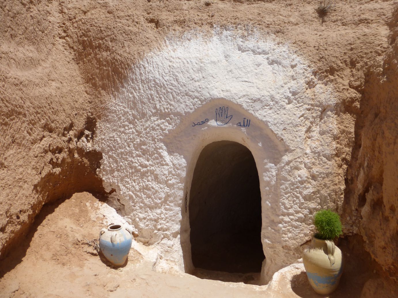 White-painted cave entrance from a Star Wars set in Tunisia, featuring a blue hand symbol, Arabic script, and two clay pots.