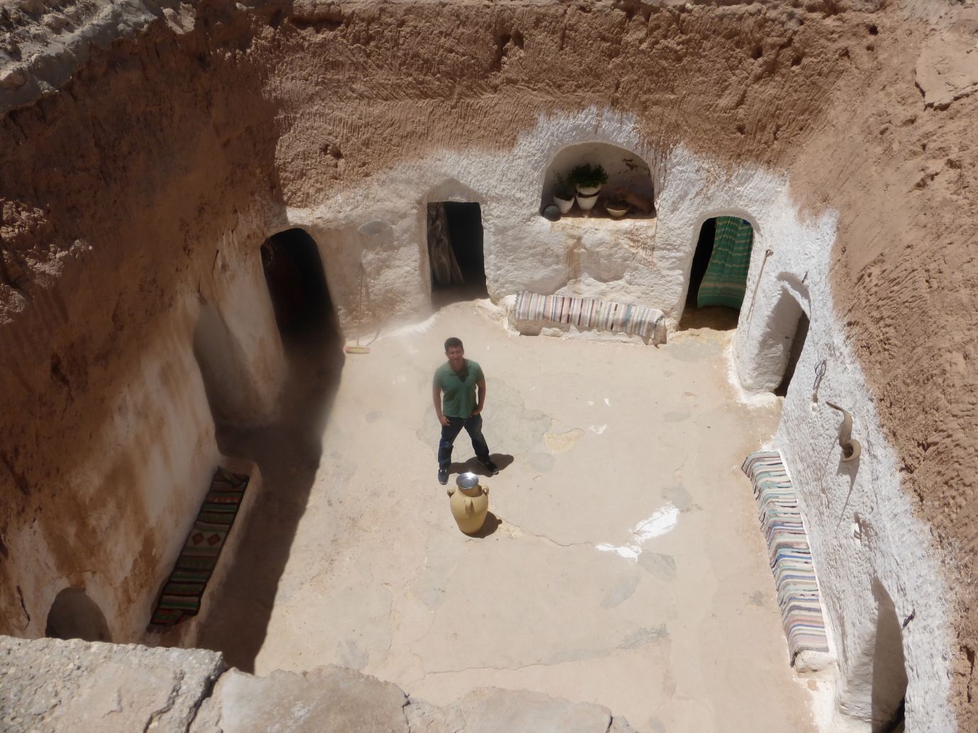 A man stands in the sandy courtyard of an original Star Wars film set in Tunisia, featuring carved rooms.