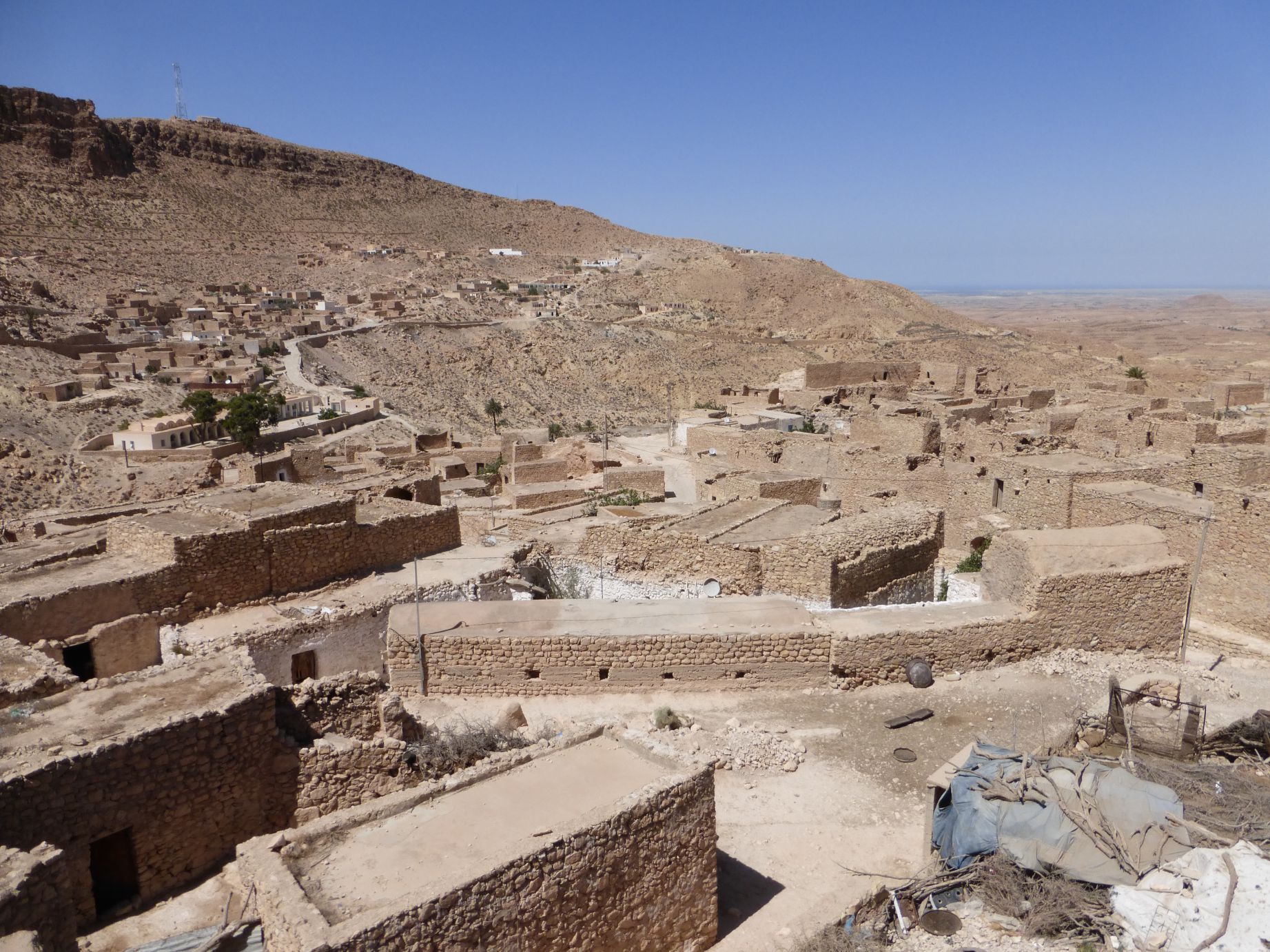 A sprawling village of light brown stone buildings covers a desert hillside under a clear blue sky, evoking a Star Wars film set.