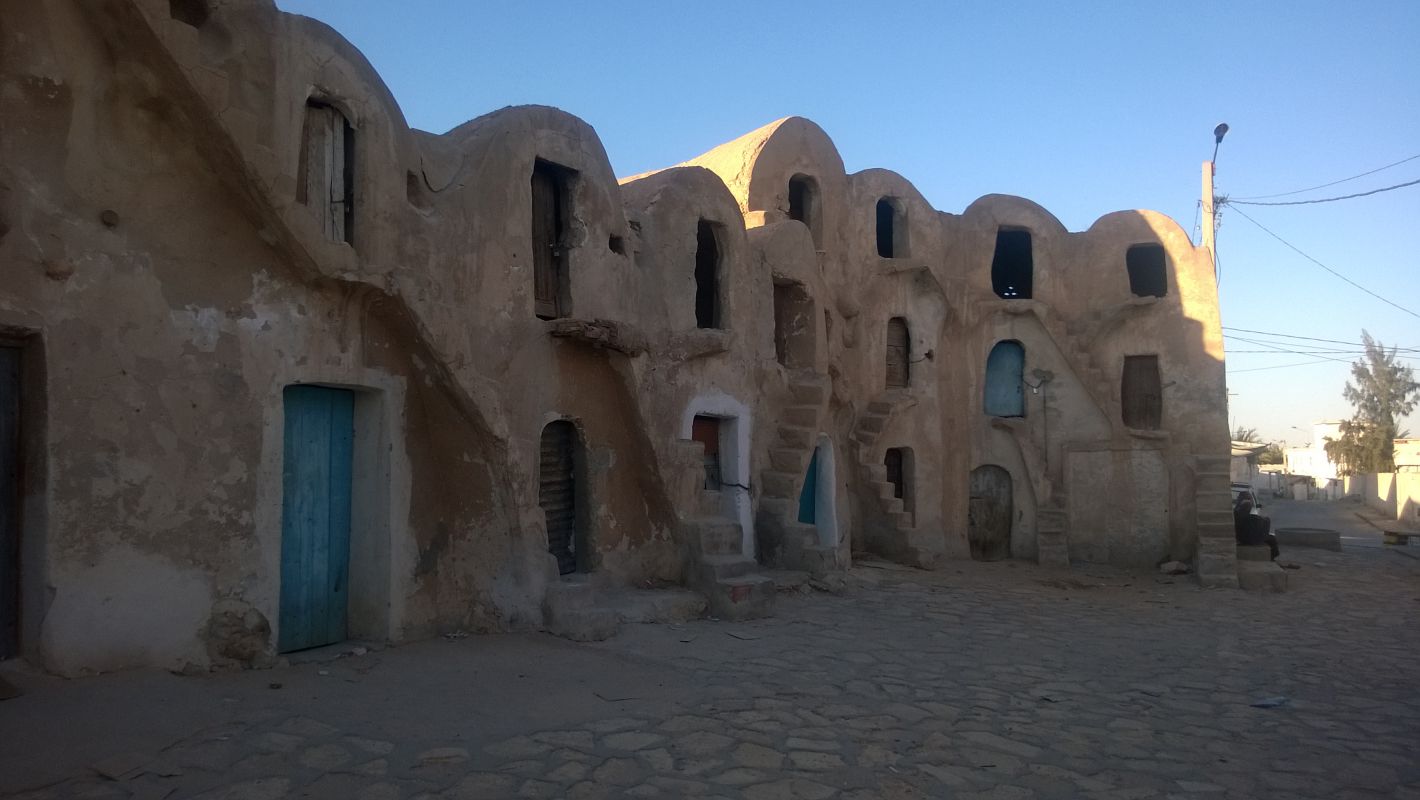 A row of ancient-looking, tan buildings with rounded roofs, multiple doorways, and small staircases, used as original Star Wars sets in Tunisia.