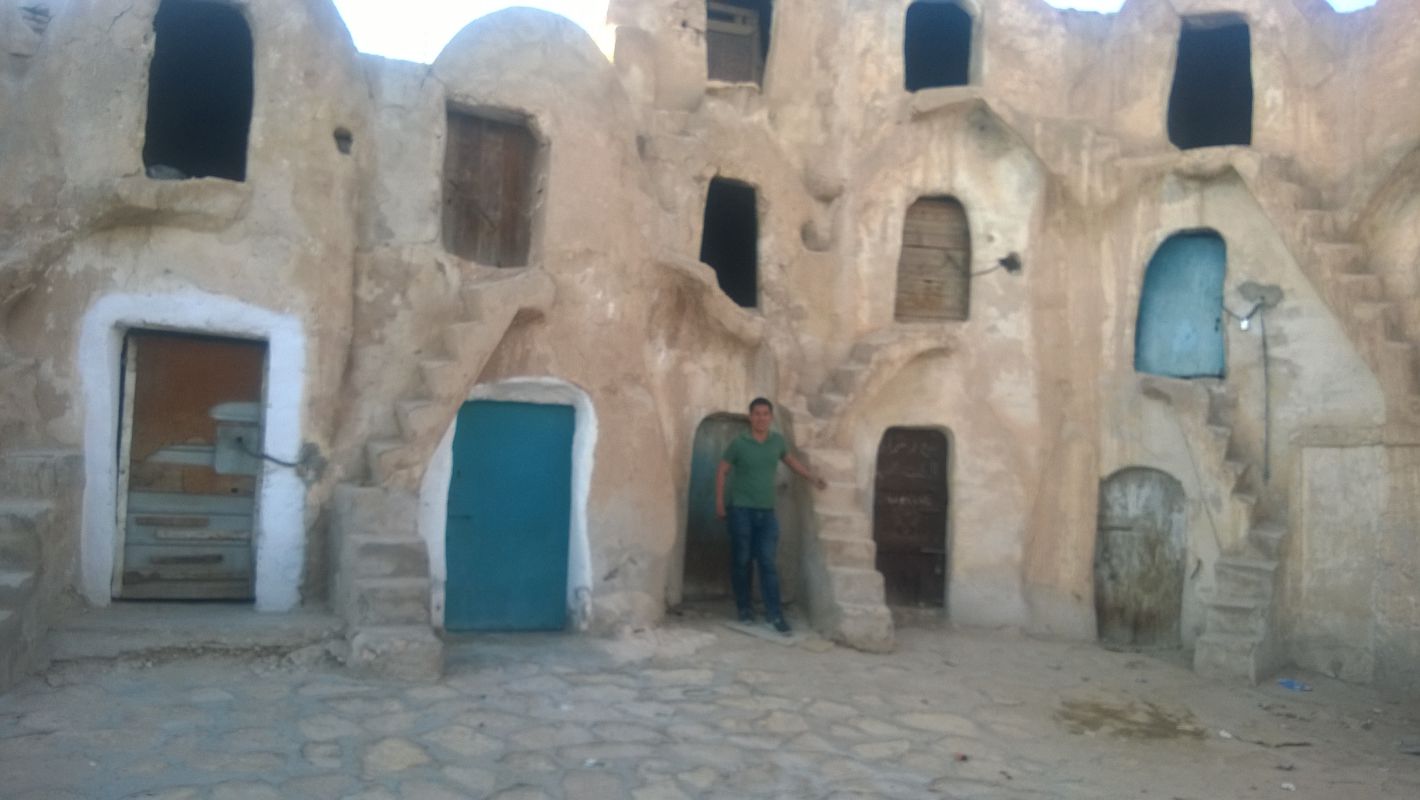 A man poses in front of a multi-level Tunisian cave dwelling, an original Star Wars film set.