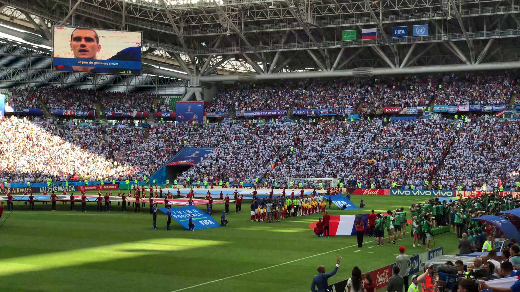 A massive crowd fills a stadium for the 2018 World Cup match between Argentina and France, with a player on the jumbotron.