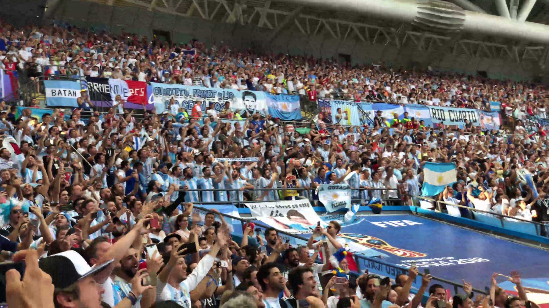 A large crowd of cheering Argentine fans fill a stadium section during the 2018 World Cup.