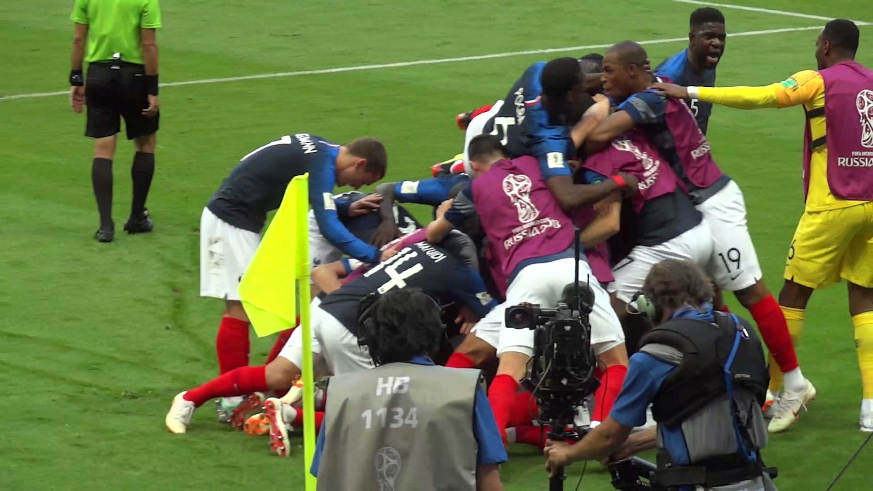 French soccer players in blue jerseys celebrate a goal by piling on each other near the corner flag at the 2018 World Cup.