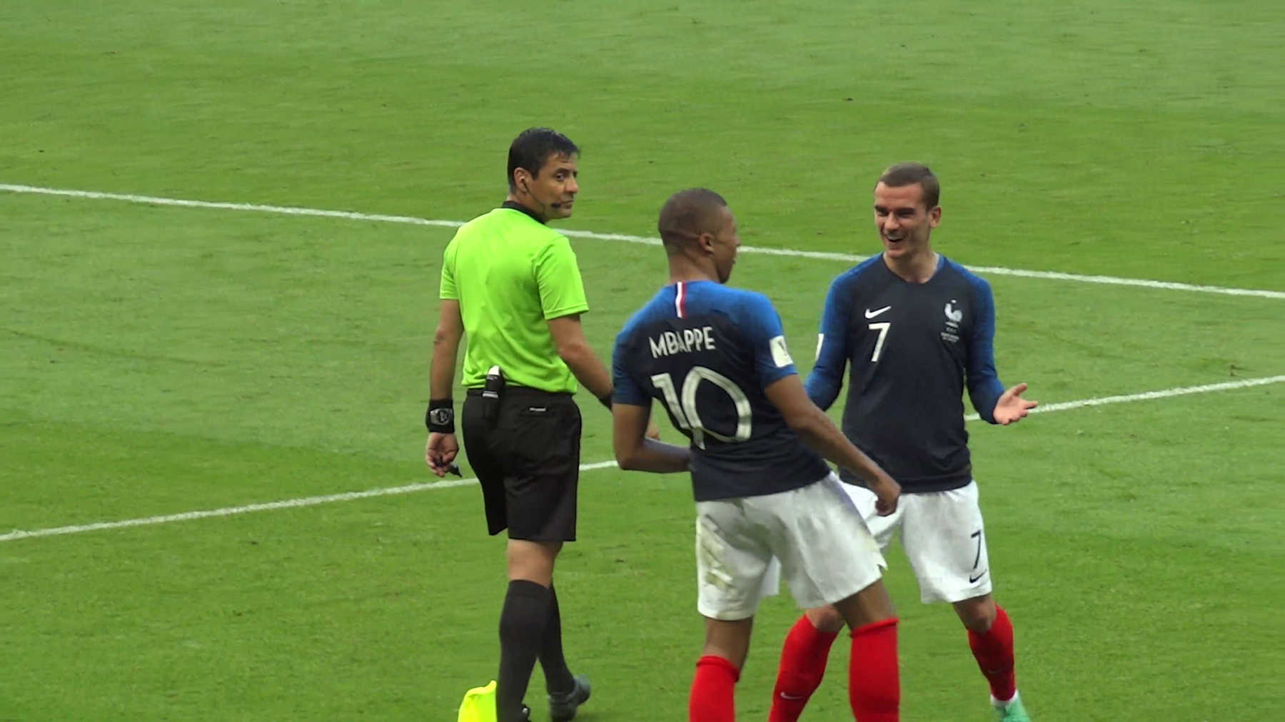 French players Kylian Mbappe and Antoine Griezmann stand near a referee on the soccer field during the 2018 World Cup.