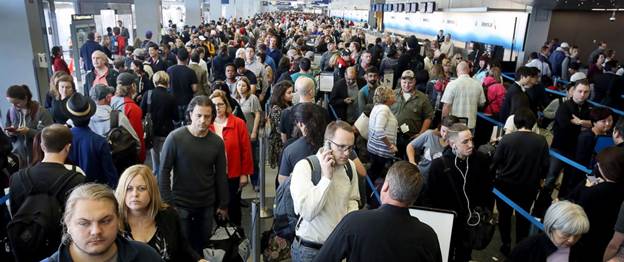 A very crowded airport terminal is filled with many travelers queueing.
