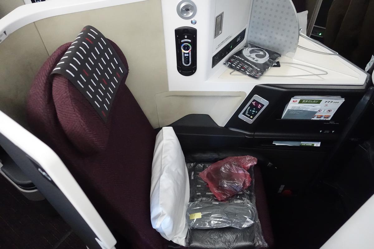 An empty Japan Airlines business class seat with a pillow, headphones, and slippers.