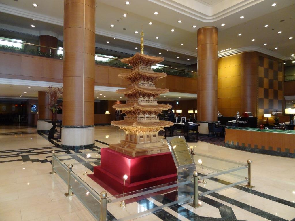A miniature, multi-tiered pagoda statue sits on a red base in a large hotel lobby.