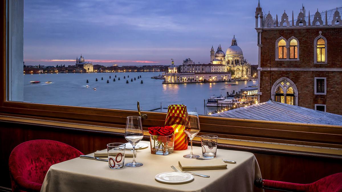 An intimate dinner table offers a stunning evening view of the illuminated Venice cityscape and Grand Canal.