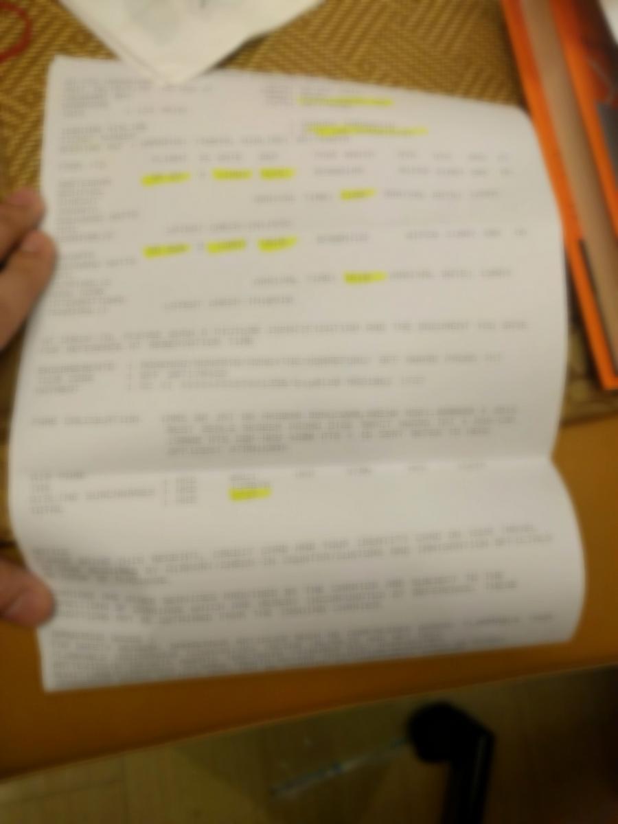 A blurry paper document, likely a flight itinerary or receipt, with yellow highlighted text.
