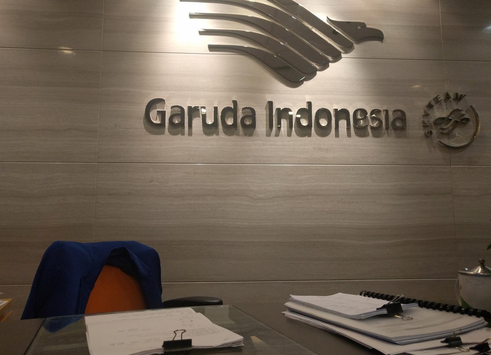 Garuda Indonesia logo and name on a wall behind a desk with papers.