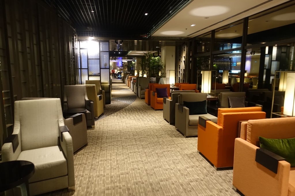 An empty, modern airport lounge with rows of armchairs in neutral, orange, and green colors.