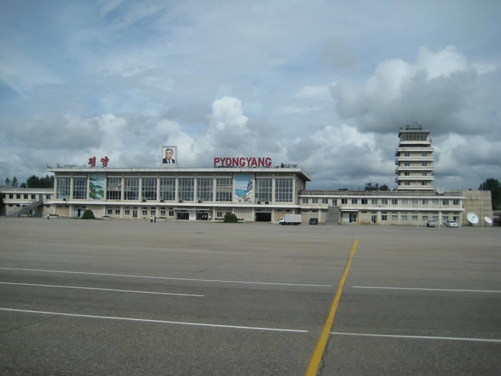 Pyongyang Airport terminal building with a portrait of a leader and a control tower, viewed from the tarmac.