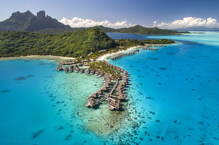 Aerial view of a luxury overwater bungalow resort in clear blue tropical waters.